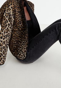 Bomberjack met luipaardprint in beige en zwart, met een doorgestikte textuur, open voorkant en zwarte accenten op de mouwen. Gecombineerd met donkere spijkerbroek.