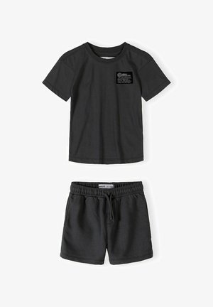 Crna majica kratkih rukava s oznakom na prsima i usklađene kratke hlače s elastičnim strukom i vezicom, položene ravno na bijelu pozadinu.