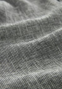 Gros plan d'un tissu à carreaux noirs et blancs avec un motif en fine grille et des plis doux créant une surface texturée et ondulée.