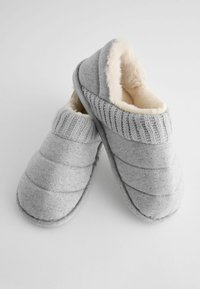 Graue gestrickte Hausschuhe mit gestepptem Design, weichem cremefarbenem Kunstfellfutter und geripptem Strickbund. Flache Gummisohle für den Innenbereich.