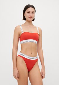Rdeča bikini komplet, ki vsebuje brezšivni bralet s belimi trakovi s Calvin Klein logotipom in ujemajoče se hlačke z visokim pasom ter pasom z logotipom.