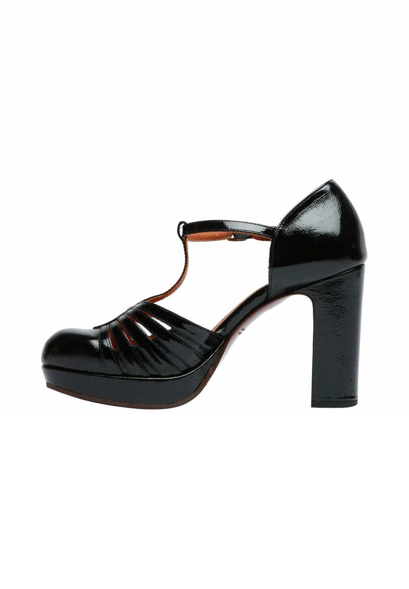 Scarpa con tacco alto in pelle verniciata nera, punta arrotondata, design a T-strap, tomaia con fessure e tacco spesso. Texture liscia con finitura lucida.