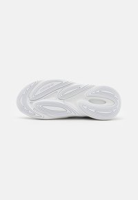 Suela de zapato blanco con goma texturizada, que presenta surcos curvados y un logo embossado. Superficie lisa con un intrincado patrón de diseño.