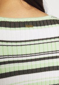 Top a coste con strisce verde, bianco e marrone, dotato di un piccolo etichetta dorata del marchio vicino al collo. Tessuto texture e design aderente.