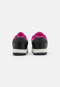 Musta urheilukengät, joissa on sileä pinta, vaaleanpunainen vuori, valkoinen kontrastipohja ja aaltoileva yksityiskohta kantapäässä. Takaviisto kuva, joka esittelee muotoilua.