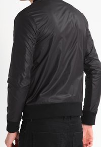 Svart bomberjacka i glänsande, lätt tyg med ribbad mudd och nederkant, med en klassisk design utan synliga mönster eller detaljer.