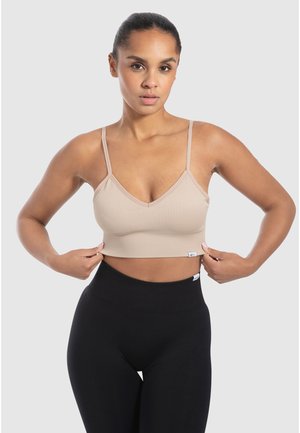 Beige geribbelde crop top met dunne verstelbare bandjes en een V-halslijn, gecombineerd met hoge zwarte leggings; zachte stof textuur.