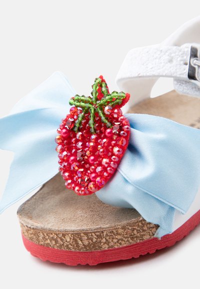 Λευκό σανδάλι με σόλα από φελλό, ανοιχτό μπλε υφασμάτινο φιόγκο και διακοσμητικό με κόκκινη χάντρα σε σχήμα φράουλας στο μπροστινό λουράκι.
