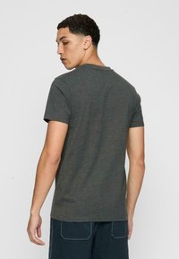 Tricou cu mânecă scurtă, de culoare gri, fabricat din țesătură moale de bumbac, având un guler rotund și o croială dreaptă, cu o textură uniformă și detalii minime.