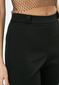 Zwarte op maat gemaakte broek met een gladde textuur, voorzien van een rechte pasvorm, zijzakken en grote zwarte knopen op de taille.