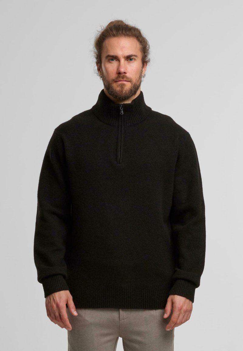 Zwarte wollen pullover met een hoge, geribbelde kraag en een rits tot halverwege. Heeft lange mouwen en een gebreide textuur.