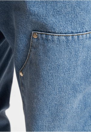 Záber zblízka na modré denimové džínsy zobrazujúce bočnú kapsu s dvoma kovovými nitmi a viditeľným šitím.