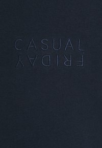 Camiseta de algodón azul marino con una textura suave, que presenta un bordado invertido del texto "VIERNES CASUAL" en un tono contrastante.
