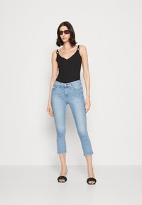 Bodysuit negro ajustado con escote en V y tirantes decorativos, combinado con jeans de mezclilla cortos de color azul claro y sandalias negras tipo deslizante.