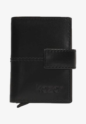 Cartera de cuero negro con una textura suave, asegurada por una correa rectangular. Presenta detalles de costura y un logo en relieve en la parte delantera.