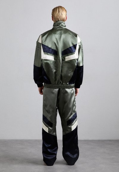 Ensemble en satin de couleur vert olive et bleu marine, avec un design en blocs de couleurs, un col haut et une taille élastique. Texture lisse, détails réfléchissants.