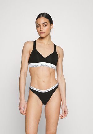 Set di bralette e perizoma in cotone nero con design a V e banda con logo Calvin Klein bianco. Texture liscia e stile minimalista.