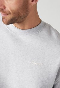 Gray sweatshirt made of cotton blend fabric, featuring a round neck, ribbed cuffs, and embroidered "Levi's" logo in light beige.