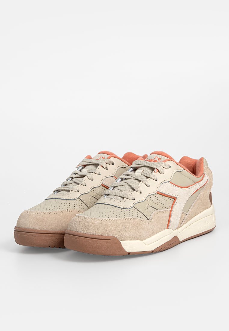 Un paio di sneaker beige e marrone chiaro con accenti arancioni, lacci allacciati e suole in gomma testurizzata su uno sfondo bianco.