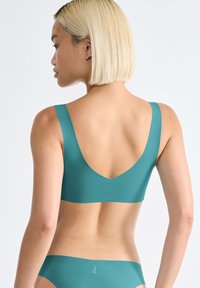 Sujeción deportiva en color azul verdoso con un amplio diseño en V en la espalda y tirantes gruesos, fabricada en material suave. Presenta un diseño minimalista, sin hardware visible ni patrones.
