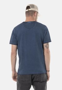 T-shirt bleu à manches courtes avec un col rond, fabriqué à partir d'un tissu doux, affichant un design de dos sans couture et une coupe décontractée.