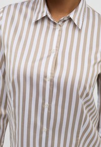 Randig skjorta med knappar i beige och vit bomullsblandning. Har en krispig krage och knäppning fram med en mjuk yta.
