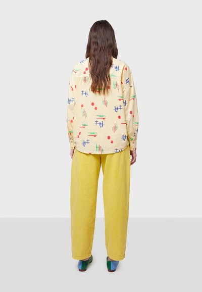 Camisa amarilla de manga larga con patrones abstractos coloridos, combinada con pantalones amarillos holgados y zapatos multicolores.