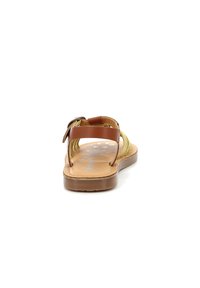 Sandalia de tira de cuero marrón con acentos de fibra natural tejida, suela plana, hebilla ajustable y plantilla texturizada con sutiles detalles impresos.