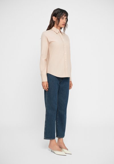 Beige long-sleeve button-up shirt, blue wide-leg jeans, and white flat shoes. The shirt has a pointed collar and subtle sheen.