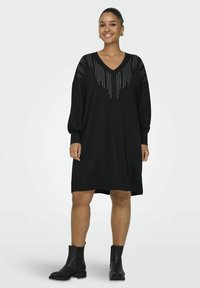 Abito nero con scollo a V e vestibilità ampia, caratterizzato da dettagli in perline d'argento decorative sulle spalle. Stivaletti neri alla caviglia completano il look.