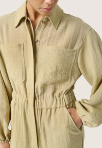 Lys grøn, struktureret stof jumpsuit med krave, knaplukning, to frontlommer og elastisk talje. Lange ærmer med samlede manchetter.