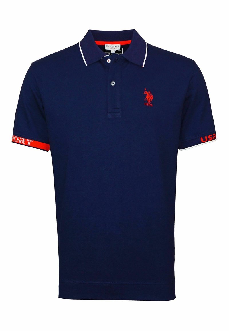 Polo bleu marine avec bordure blanche au col, logo USPA rouge sur la poitrine, texte rouge et blanc sur les poignets des manches, et patte de boutonnage à deux boutons.