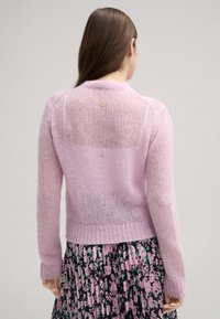 Rosa gestrickte Strickjacke mit loser Textur, ausgestattet mit gerippten Bündchen und Saum. Kleines Logodetail auf dem oberen Rücken.