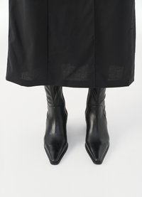 Botine negre din piele, cu vârful ascuțit, având o textură netedă și un design ajustat. Marginile din țesătură sunt vizibile deasupra botinelor.