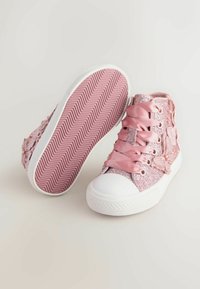 Różowe błyszczące sneakersy typu high-top z satynowymi sznurówkami, kwiatowymi akcentami i białym gumowym czubkiem. Teksturowana różowa podeszwa z wzorem w zygzak.