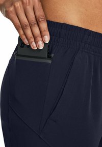 Navy pants with elastic waistband feature a zippered pocket holding a black smartphone, highlighting a sleek, functional design.