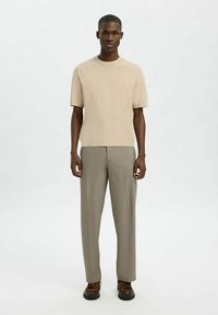 Bežinis trumpomis rankovėmis megztinis, apvaliu iškirpimu, derinamas su šviesiai pilkais kelnėmis. Rudi batai su raišteliais ir masyviu padu. Minimalistinis dizainas.