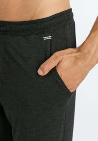 Donkergrijze loungebroek van zacht materiaal, met een zijzak en een elastische tailleband met een klein label waarop "HANRO" staat.