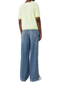 Limoengroene gestreepte shirt met korte mouwen, gecombineerd met wijde blauwe jeans. Het shirt heeft een ronde halslijn en een ribbelrand. Casual en ontspannen pasvorm.