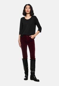 Schwarzes Oberteil mit drei Viertelärmeln, bordeauxfarbene Cord-Hose und schwarze kniehohe Stiefel. Das Outfit hat eine lockere Passform und einen strukturierten Stoff.