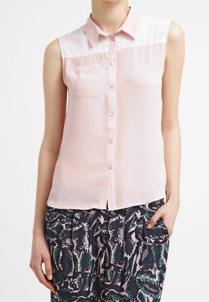 Lichtroze mouwloze blouse met knoopsluiting aan de voorkant, zakdetail en witte panelen op de schouders. Zacht, doorschijnend materiaal.