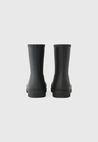 Bottes de pluie en caoutchouc noir avec une texture lisse, un tige haute et des rainures verticales subtiles, dotées d'une semelle discrète et d'un logo en relief.