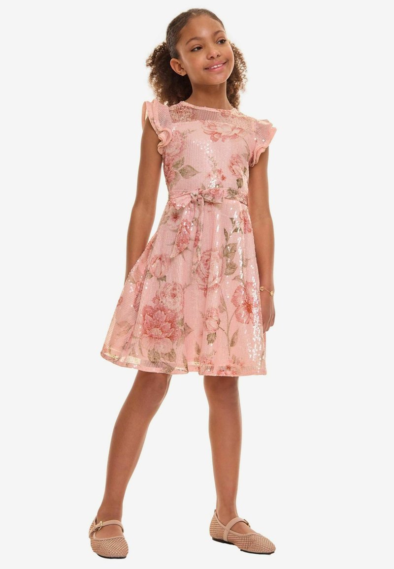 Rochie roz cu model floral, cu mâneci scurte și volane, cu textură strălucitoare și curea la talie. Asortată cu încălțăminte bej cu broderie.