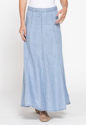 Gonna lunga in denim azzurro chiaro indossata con ballerine beige intrecciate e top bianco, mostrata dalla vita ai piedi su uno sfondo semplice.