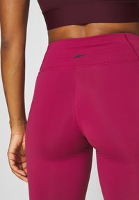 Magenta atletiska leggings med hög midja, med en liten svart logotyp på baksidan. Slät och stretchig tyg med platta sömmar.
