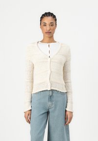 Knit cardigan in off-white, featuring a V-neck, long sleeves, and button closure. Textured pattern, cropped length, and ribbed hem.