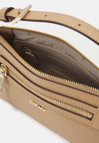 Bolsa DKNY em tom dourado, com hardware em tom dourado, apresentando compartimentos com zíper, um acabamento texturizado e uma alça ajustável. O interior inclui bolsos.
