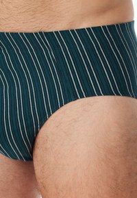 Slip da bagno da uomo in tessuto verde scuro con sottili strisce bianche. La vita è elasticizzata e il materiale sembra morbido con una texture liscia.