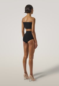Completo da bagno a due pezzi nero a bandeau con slip alta vita, caratterizzato da una texture liscia e un design minimalista. Tacchi alti nude completano l'outfit.