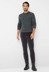 Grau gestrickter Pullover mit gerippten Manschetten, kombiniert mit dunklen Cordhose und schwarzen geschnürten Stiefeln. Einfaches Design und strukturierter Stoff.